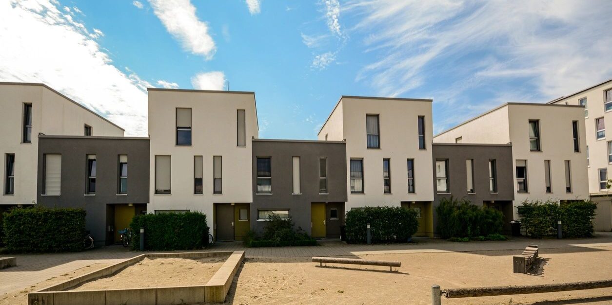 A row of houses on the sand in front of some trees.